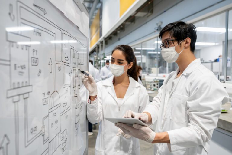 STEM lab partners wearing facemasks and checking a process using a white board